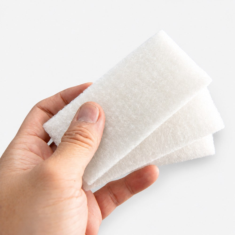 Two AquaFin polyester floss pads held in a hand