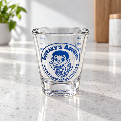 Squeaky's Aquatics Measuring Glass, clear 1 oz glass dosing cup with blue mascot logo and measuring scales